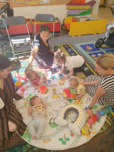 Lancaster group, shows parents and baby sat round chatting and playing 